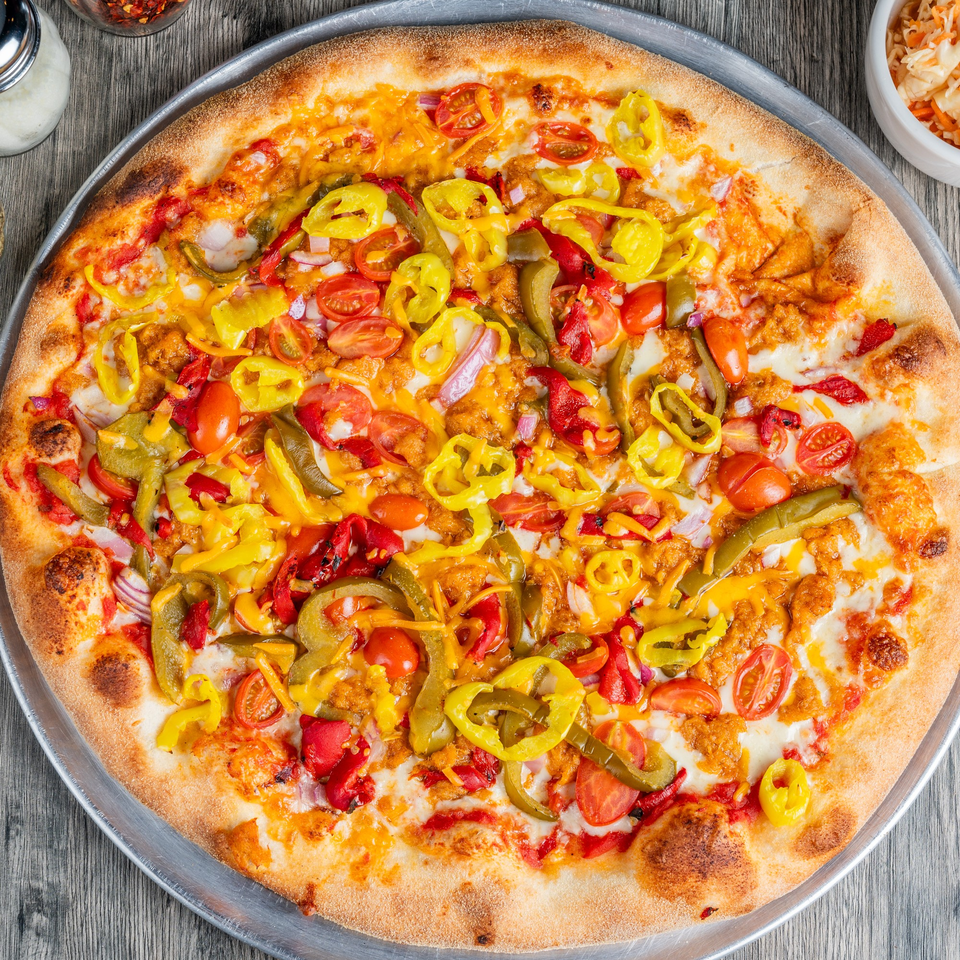 Fantasy Pizza's colorful pizza with red and yellow peppers, tomatoes, and onions on a metal tray.