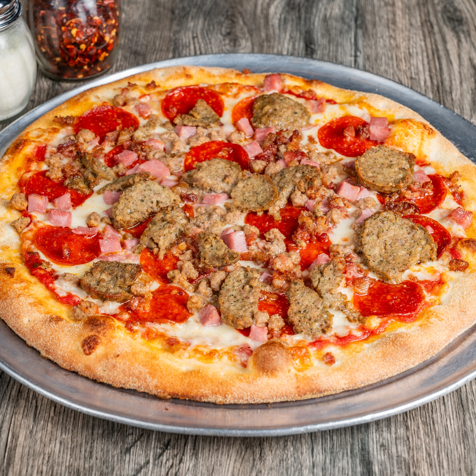 Fantasy Pizza's meat lover's pizza, topped with pepperoni, sausage, and ham, on a metal tray.