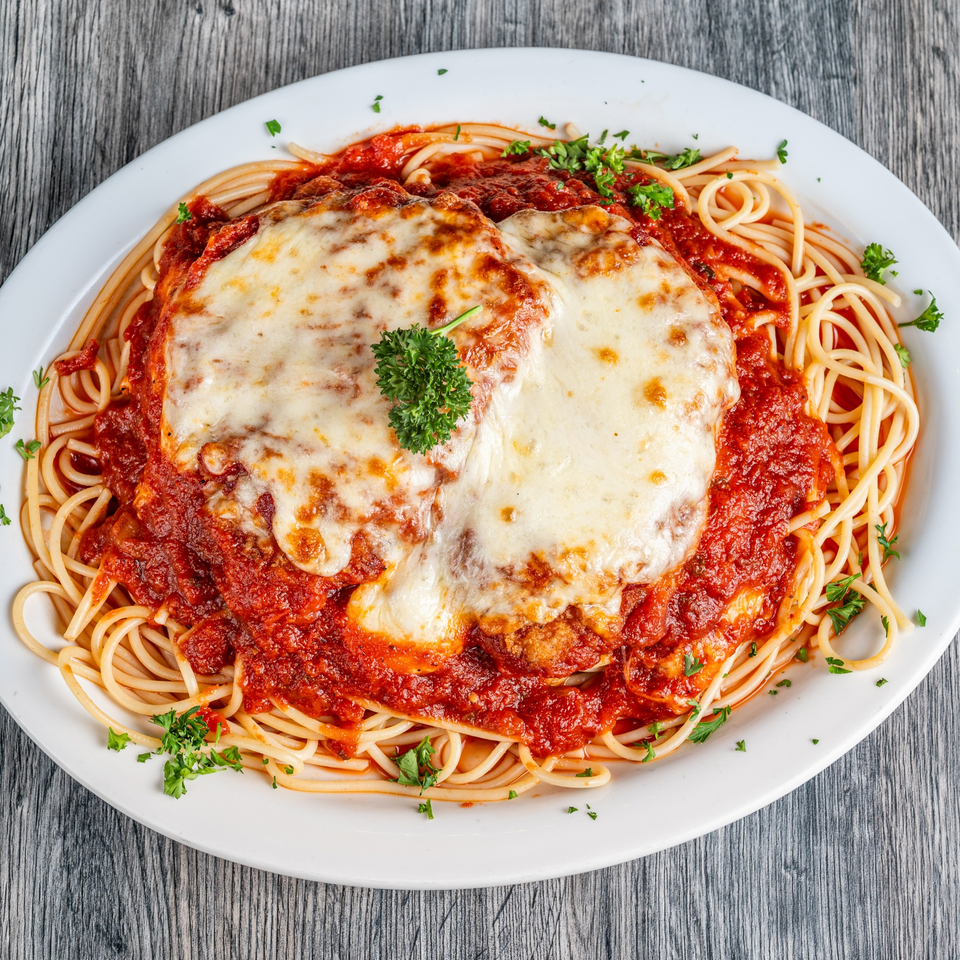 Chicken Parmesan with spaghetti and red sauce, topped with melted cheese and parsley.