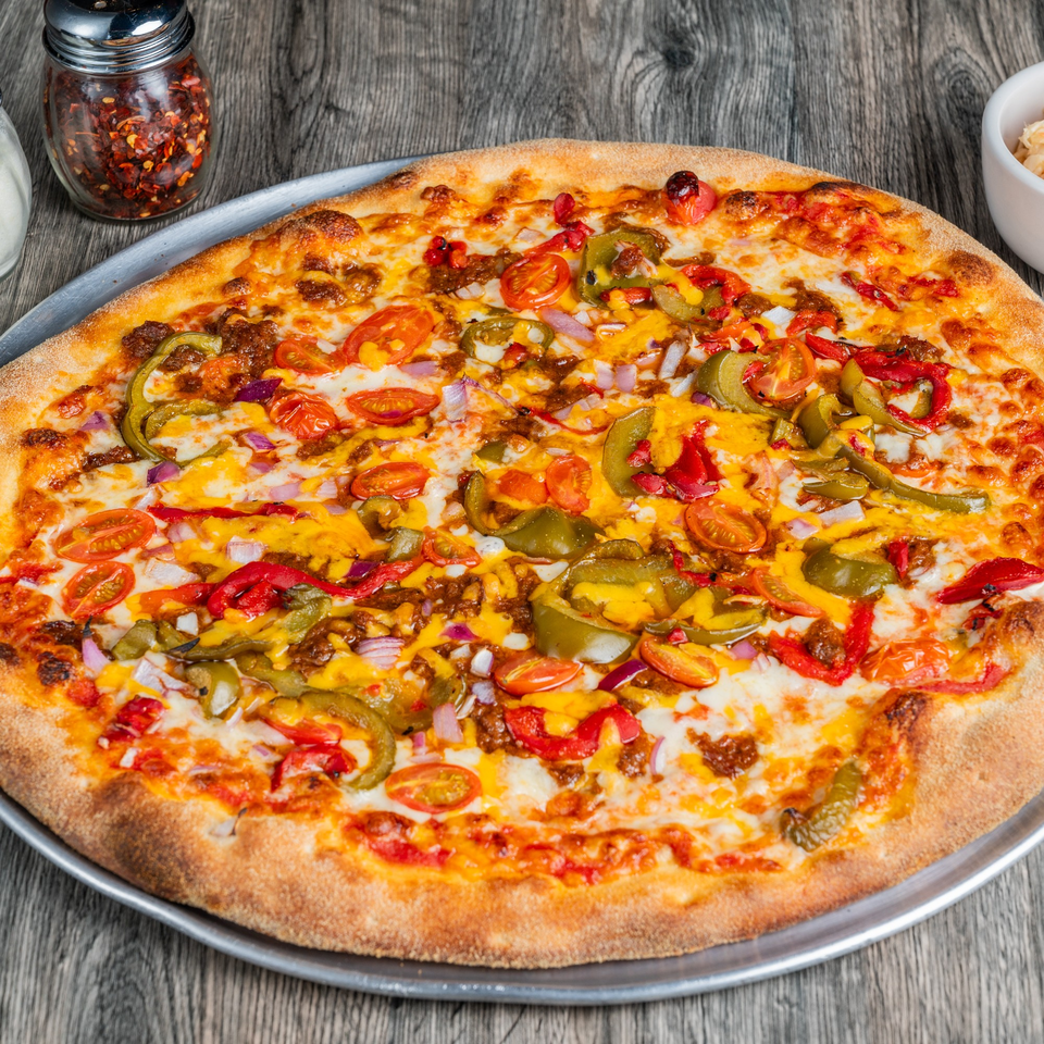 A Fantasy Pizza with chili, cheese, red onions, tomatoes, and green peppers on a metal tray.