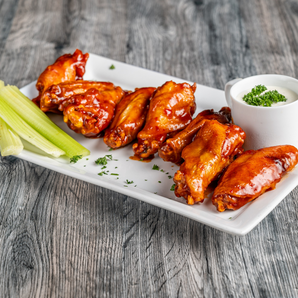 Fantasy Pizza's buffalo wings, celery sticks, and ranch dressing on a white rectangular plate.